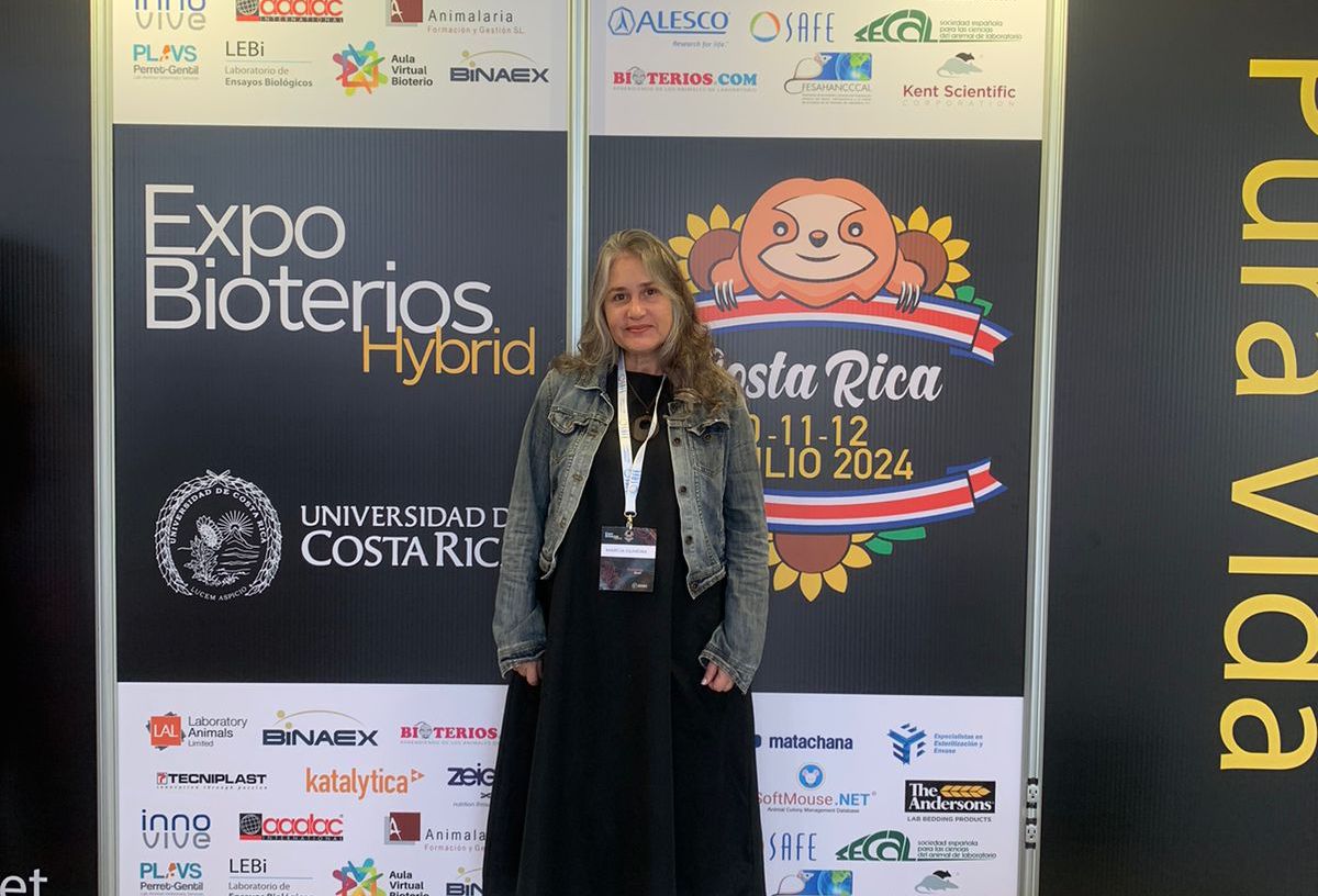 Márcia Oliveira, chefe do SCQA/ICTB, posa em frente ao painel de divulgação do ExpoBioterios Hybrid 2024